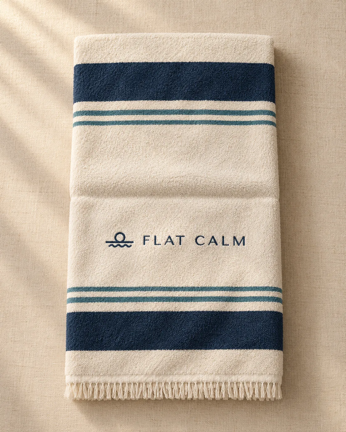 Folded sand beach towel with navy stripes and the Flat Calm logo